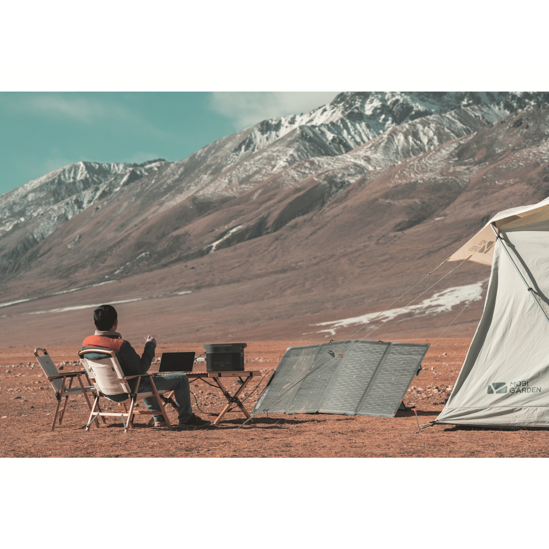 Osoba biwakująca w górach. Laptop, jedzenie i panel słoneczny na stole i krześle.
