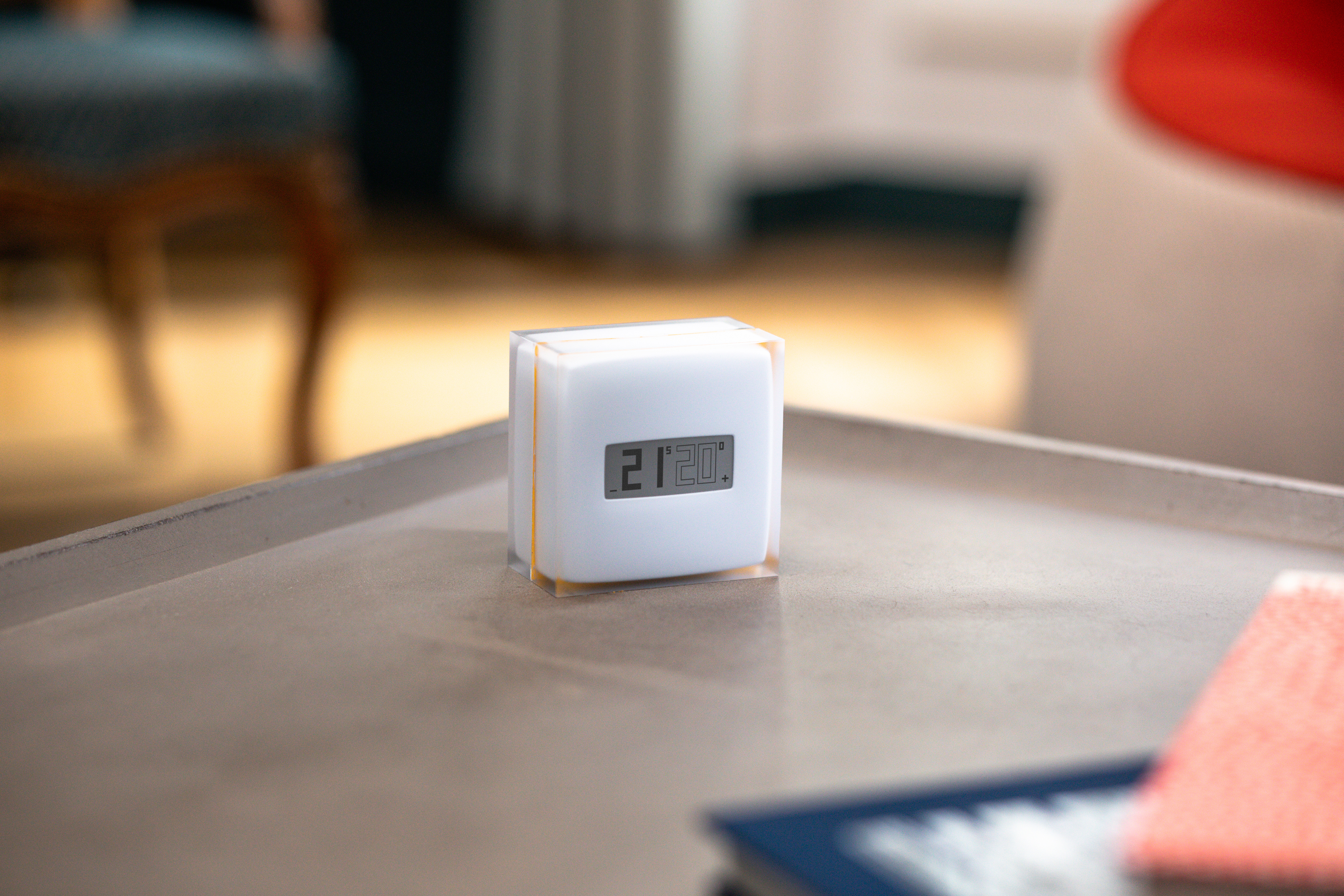 A white cube-shaped device with a digital display on a table, showing the time 21:20. A blue book visible.