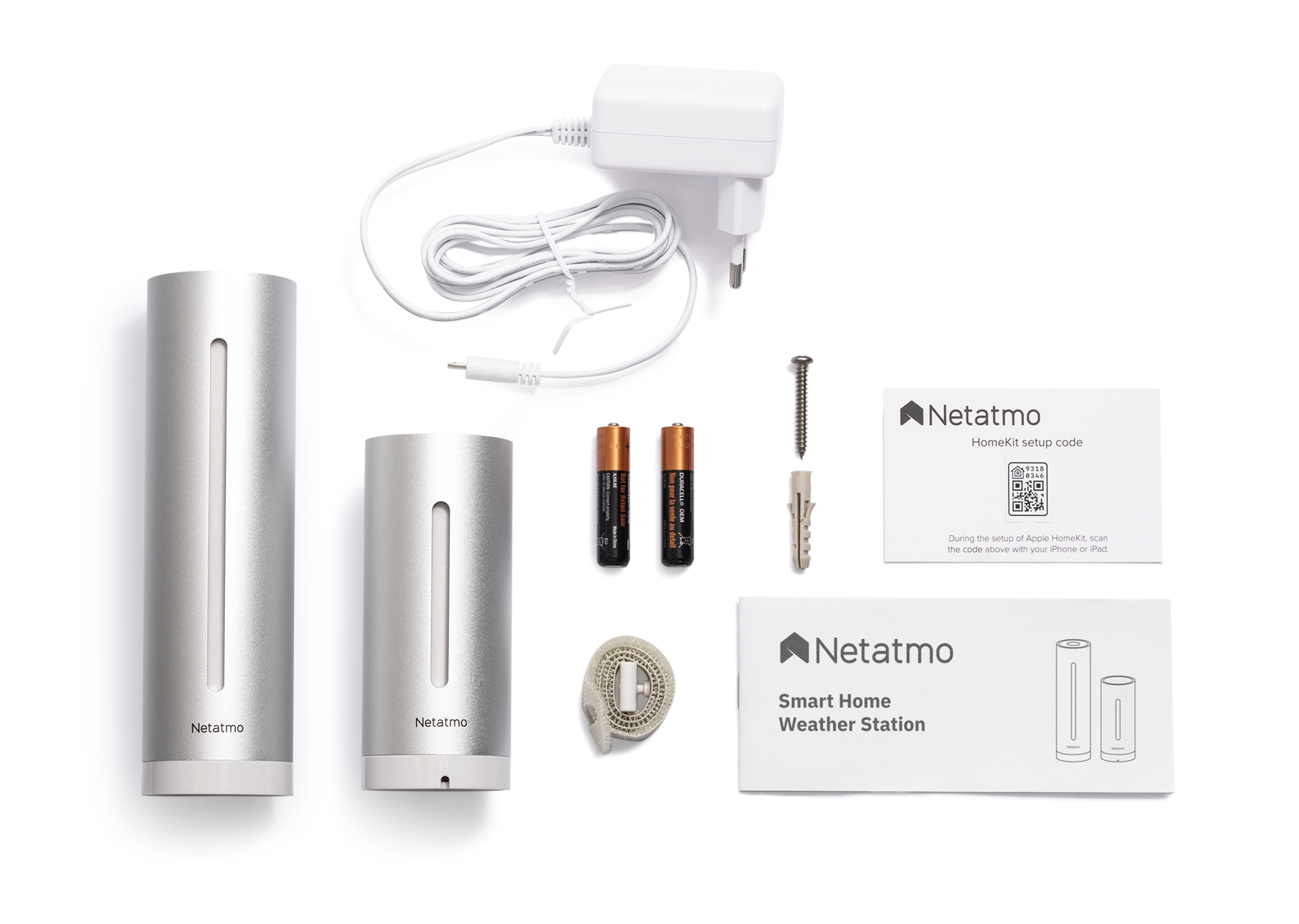 Weather station components: two silver cylinders, batteries, and a setup guide on a white surface.