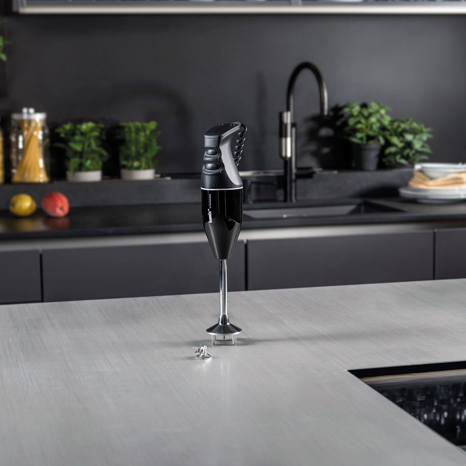 Un frullatore a immersione nero su un piano di lavoro grigio in un ambiente cucina moderno.