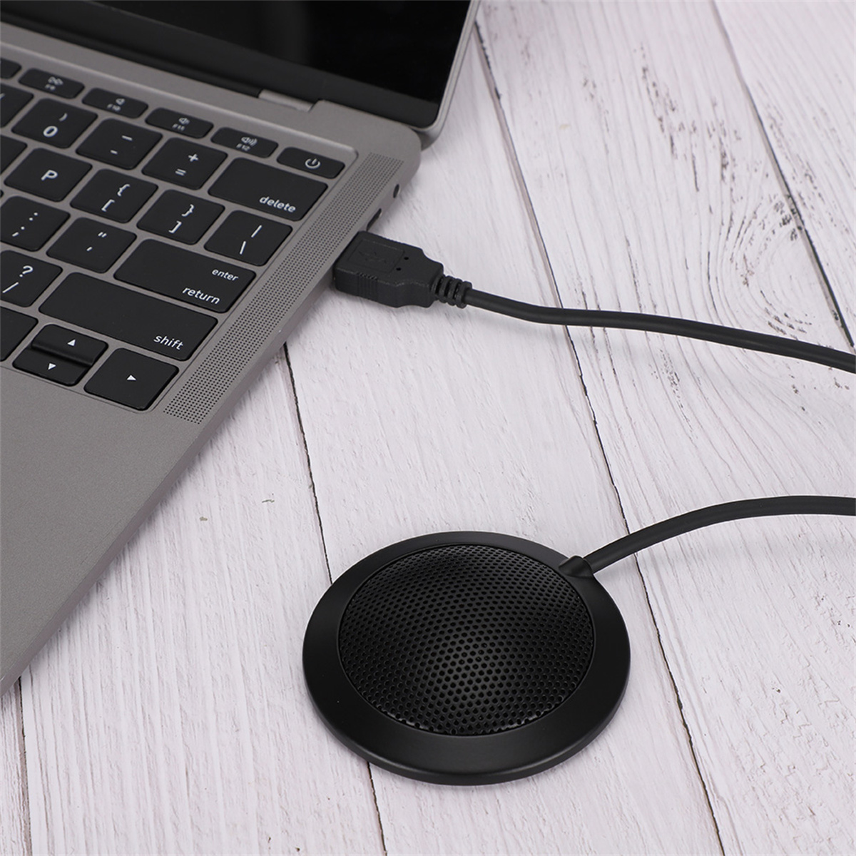 Laptop mit angeschlossenem USB-Mikrofon. Schwarzes Mikrofon auf weißer Holzoberfläche.