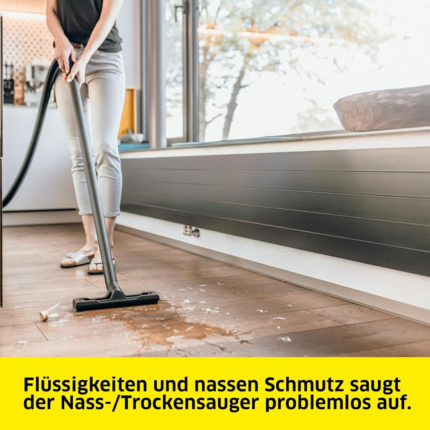 Eine Frau saugt einen Holzboden. Auf dem Boden befindet sich eine verschüttete Flüssigkeit. Text darunter.