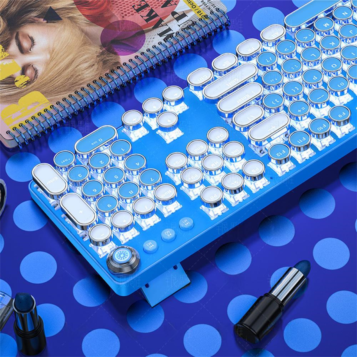 Eine blaue Tastatur im Retro-Stil mit runden Tasten, ein Notizbuch und Lippenstift auf blauem Tupfenhintergrund.