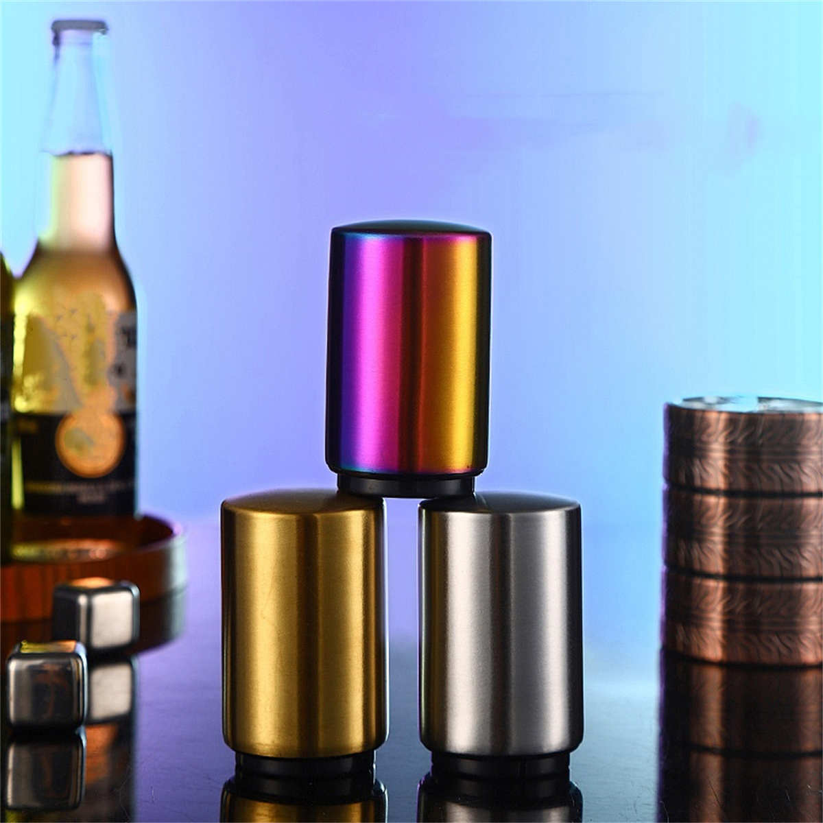 Drei metallische Flaschenöffner in verschiedenen Farben. Eine Flasche Bier befindet sich im Hintergrund.
