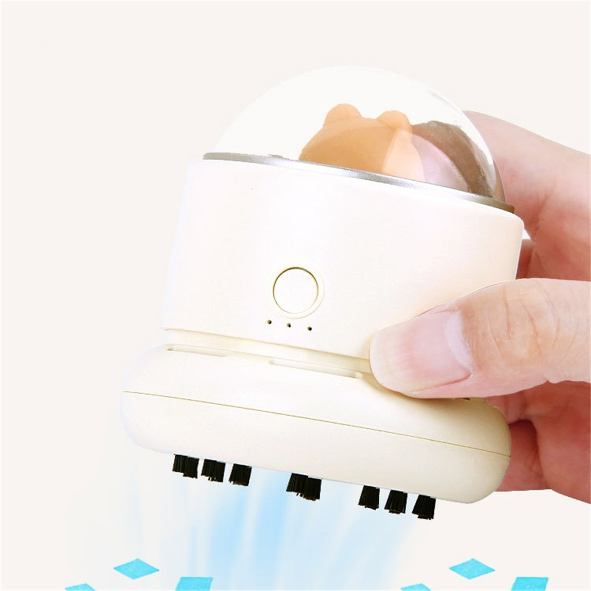 Ein Mini-Staubsauger mit einer Bärenfigur in einer transparenten Kuppel. Eine Hand hält das Gerät, blaue Flecken drumherum.