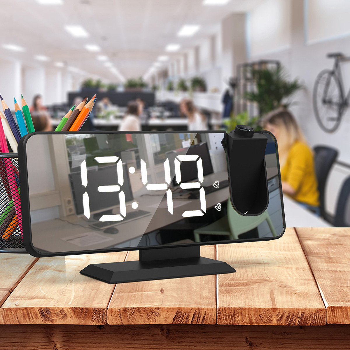 Schwarze Uhr auf einem Holztisch. Die Uhr zeigt die Zeit 13:49 an. Der Hintergrund ist ein Büro.