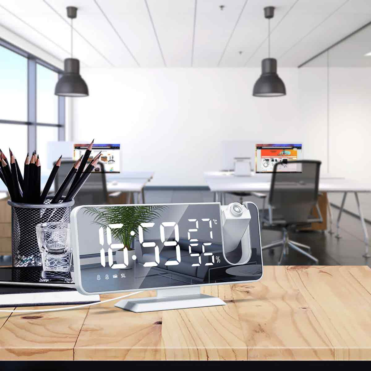 Eine Digitaluhr, die Zeit und Temperatur auf einem Holzschreibtisch in einem Büroumfeld anzeigt.