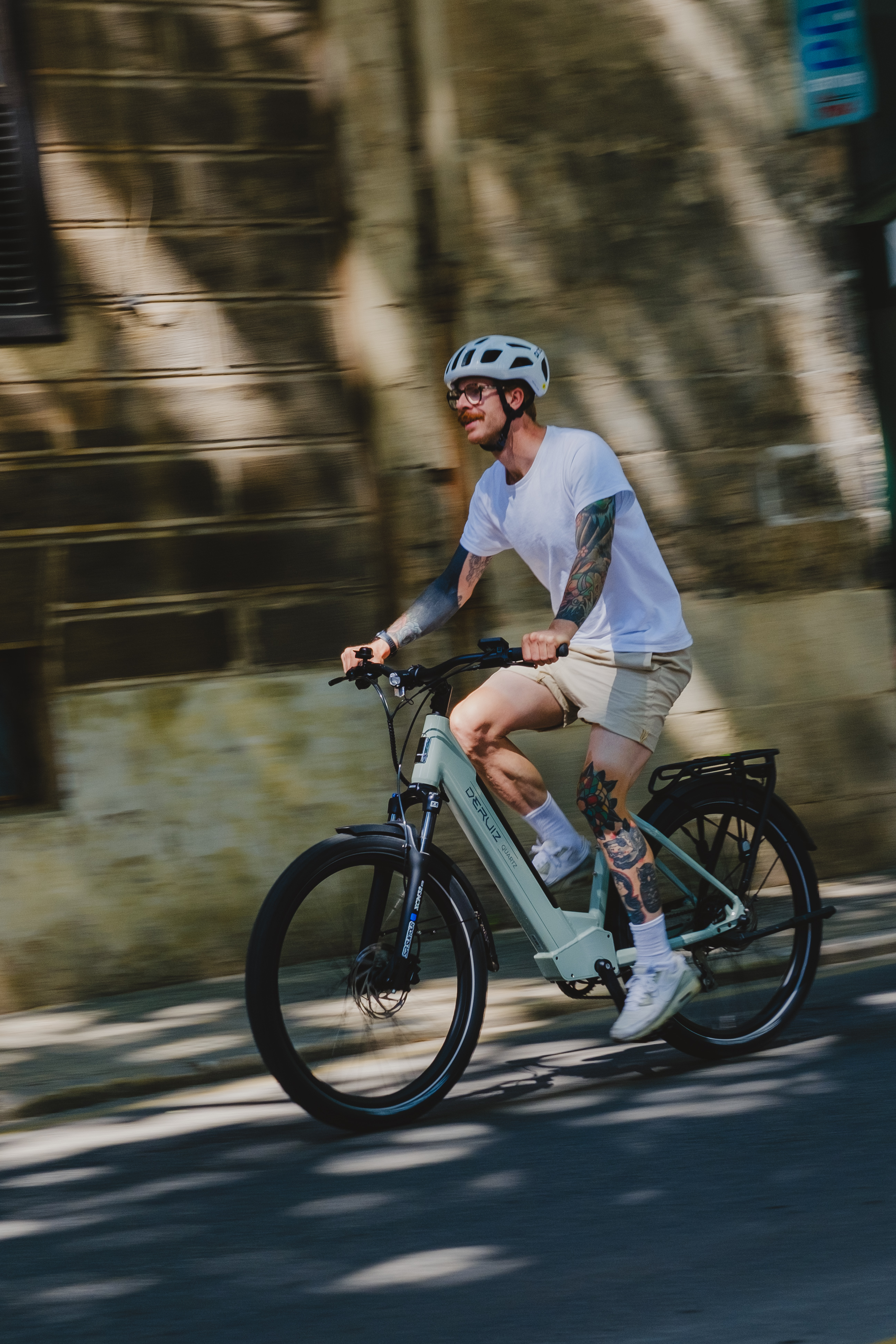 Mann fährt auf einer grünen E-Bike auf einer Straße. Er trägt einen Helm und hat Tätowierungen auf den Armen.