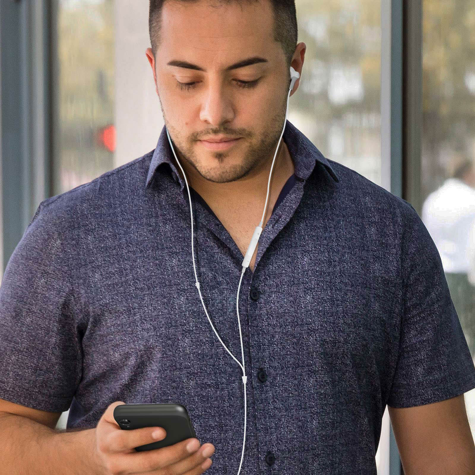 Un hombre con camisa azul marino sostiene un teléfono negro y tiene auriculares blancos en las orejas.