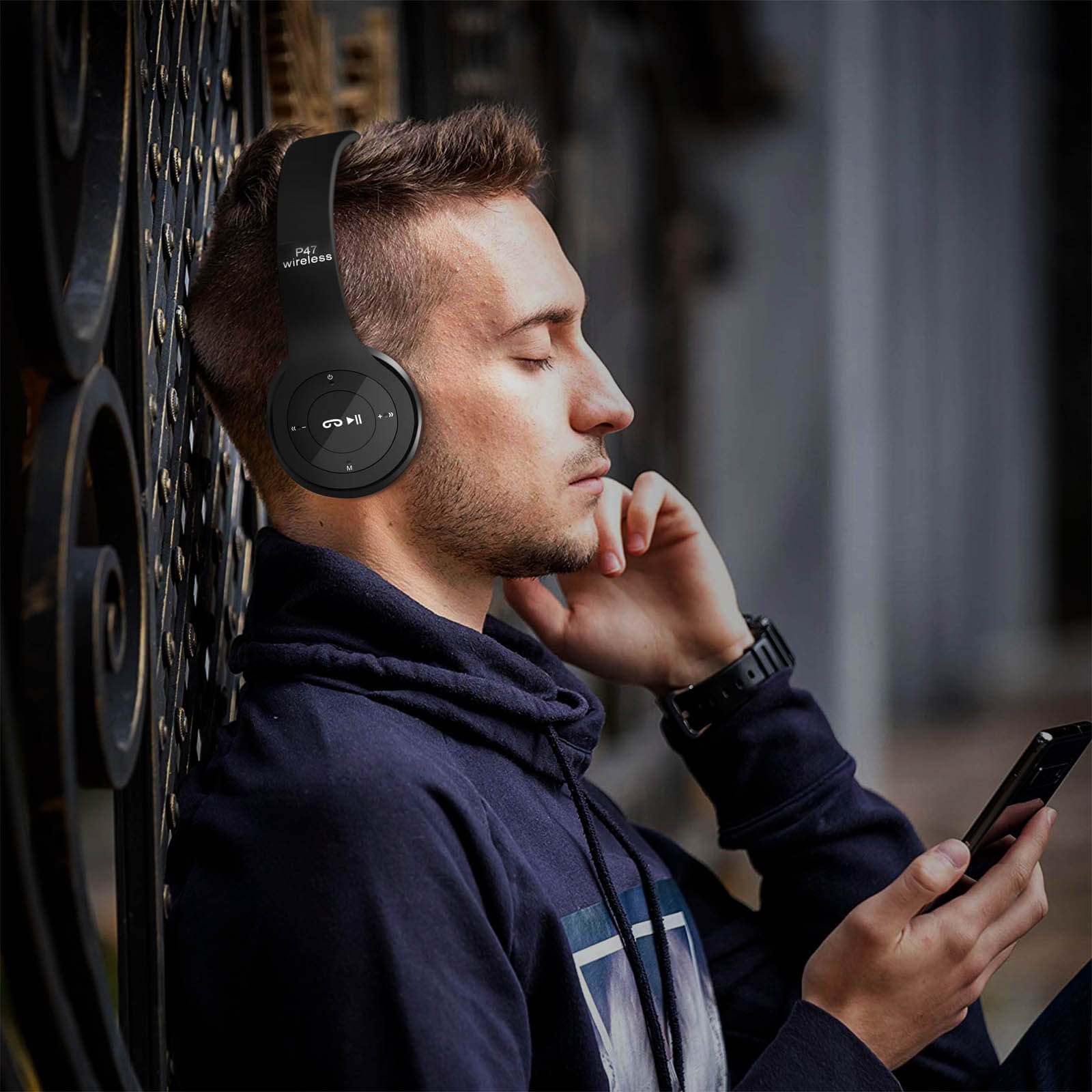 Homme portant un casque noir, adossé à une porte, tenant un téléphone, les yeux fermés.