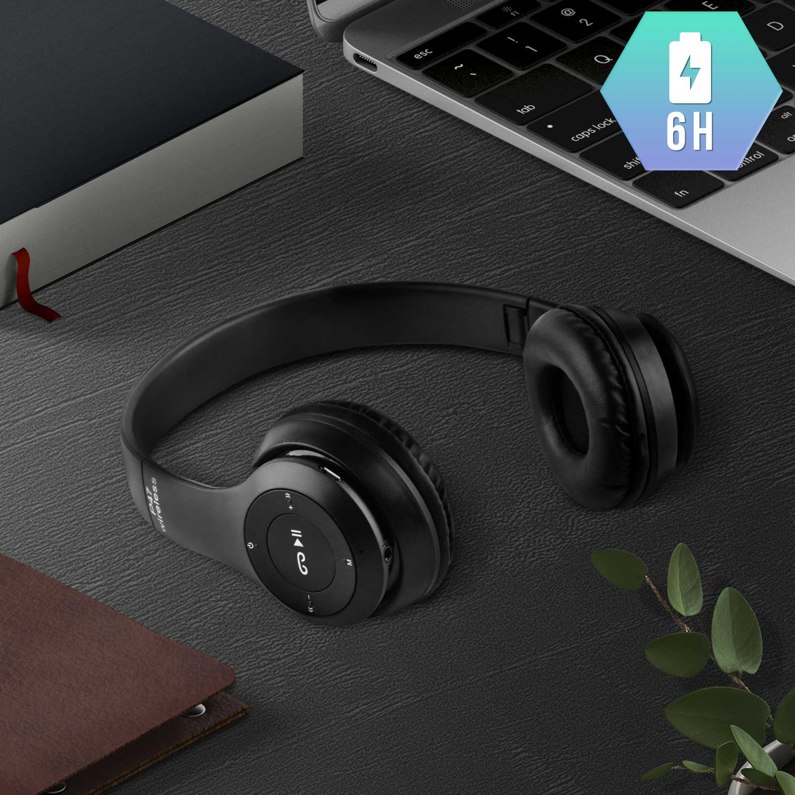 Casque sans fil noir sur un bureau sombre. Ordinateur portable et livre en arrière-plan.