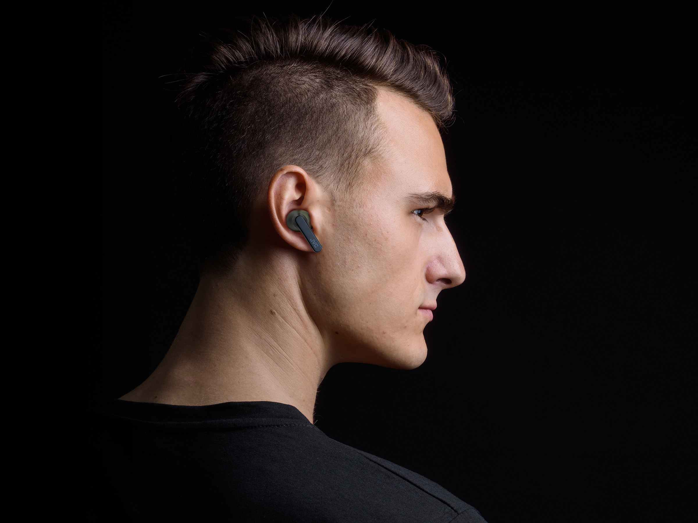 Un uomo con un auricolare nell'orecchio, ripresa di profilo. Indossa una camicia nera.