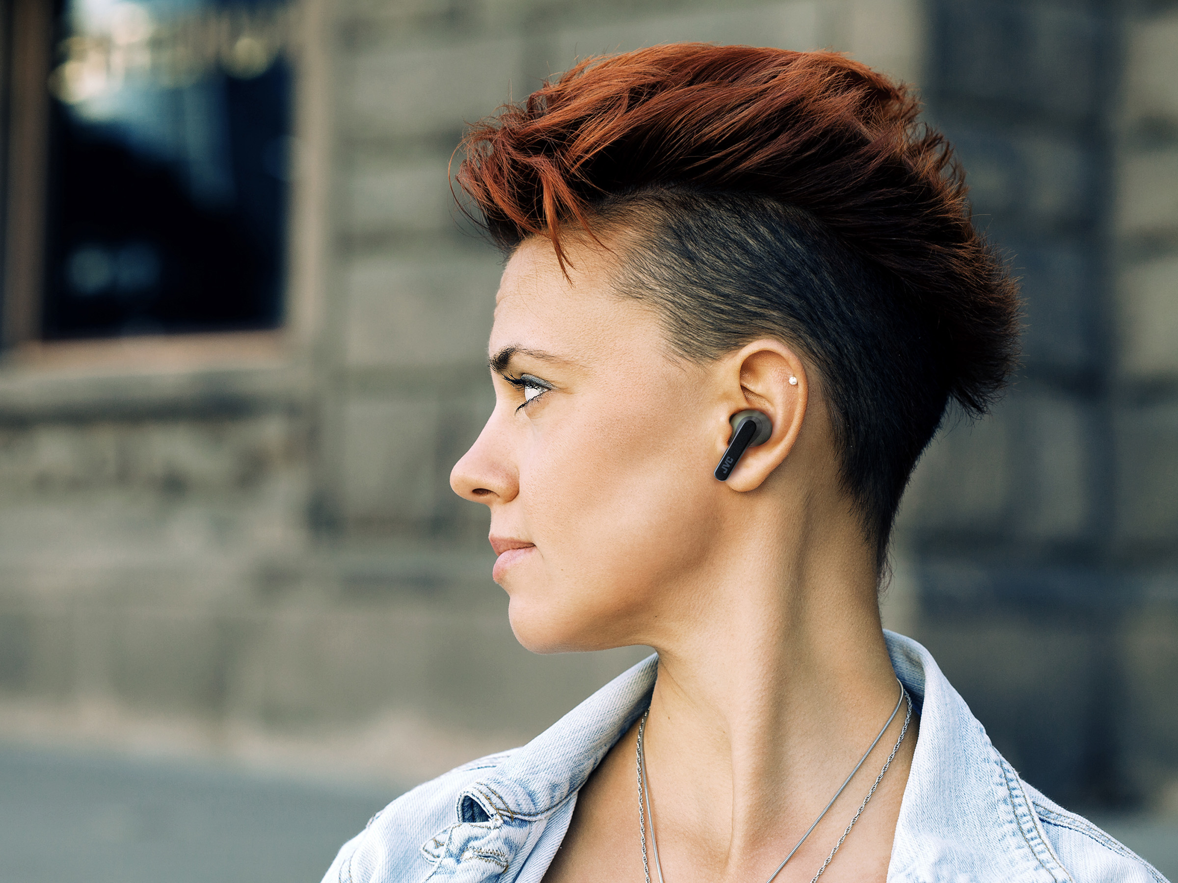 Donna con auricolare nero nell'orecchio. Capelli rossi corti. Sfondo strada sfocata.