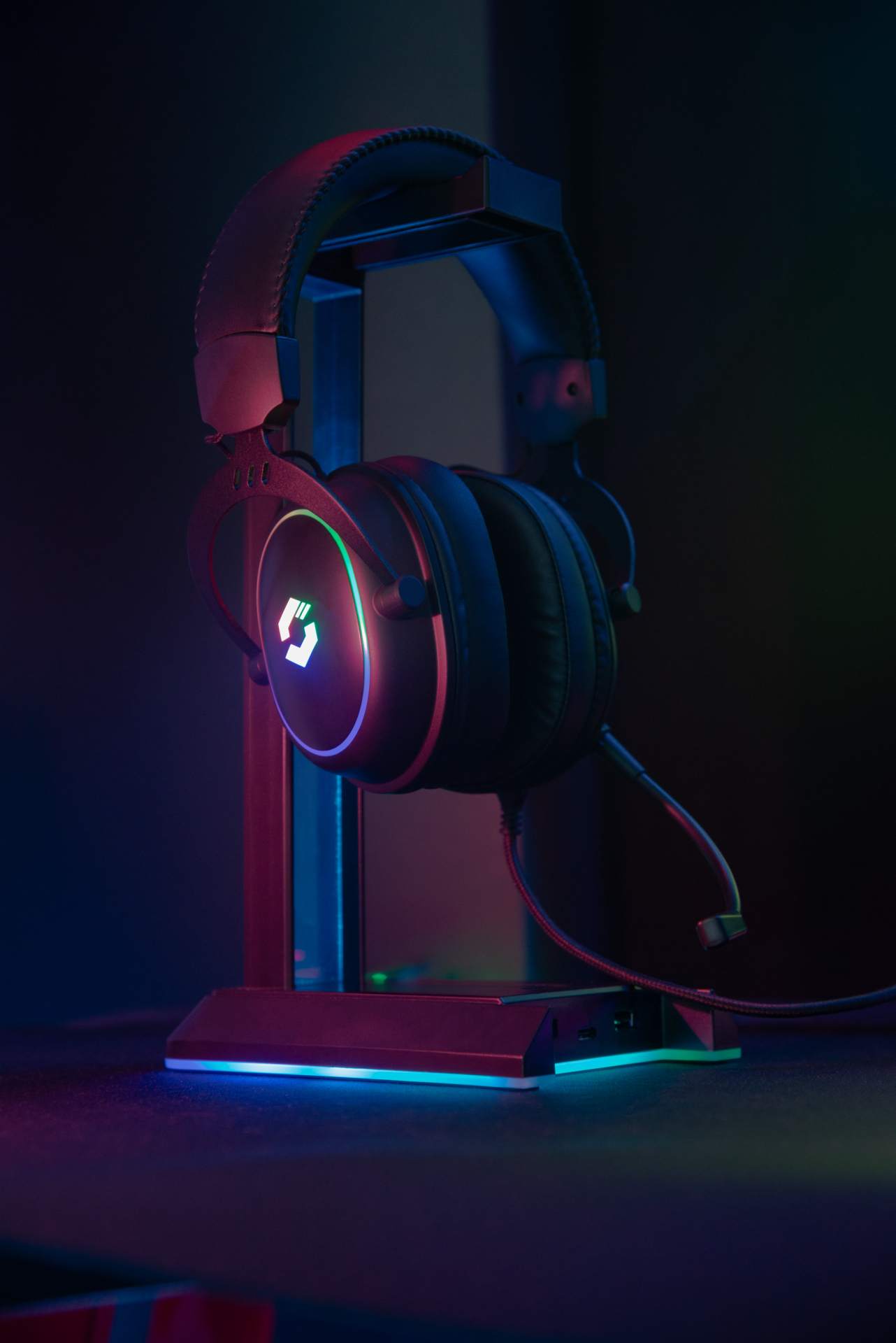 Schwarzes Gaming-Headset auf einem Ständer, beleuchtet mit roten, grünen und blauen Lichtern. Dunkler Hintergrund.