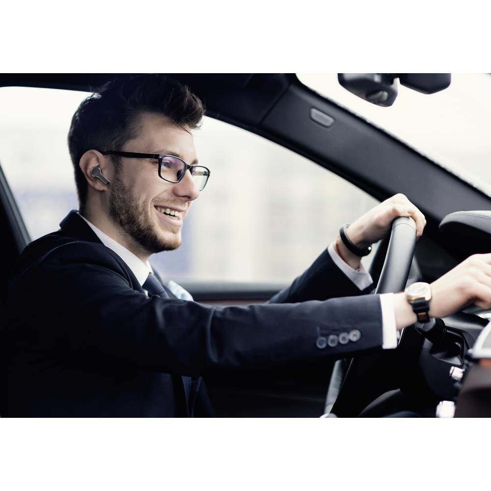 Ein Mann im Auto mit Ohrhörern, lächelt, mit den Händen am Lenkrad.