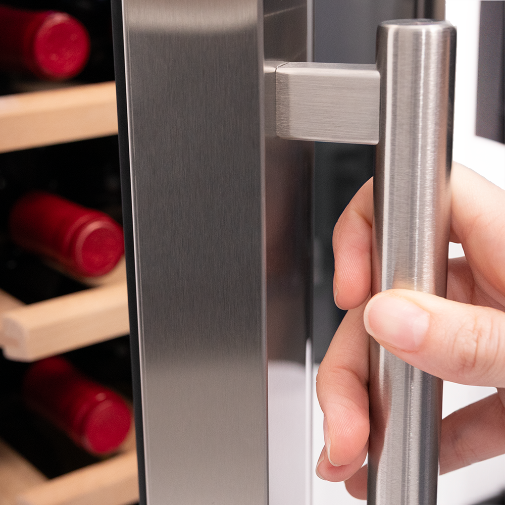 Hand holding a stainless steel door handle, close up. Red wine bottles visible inside.