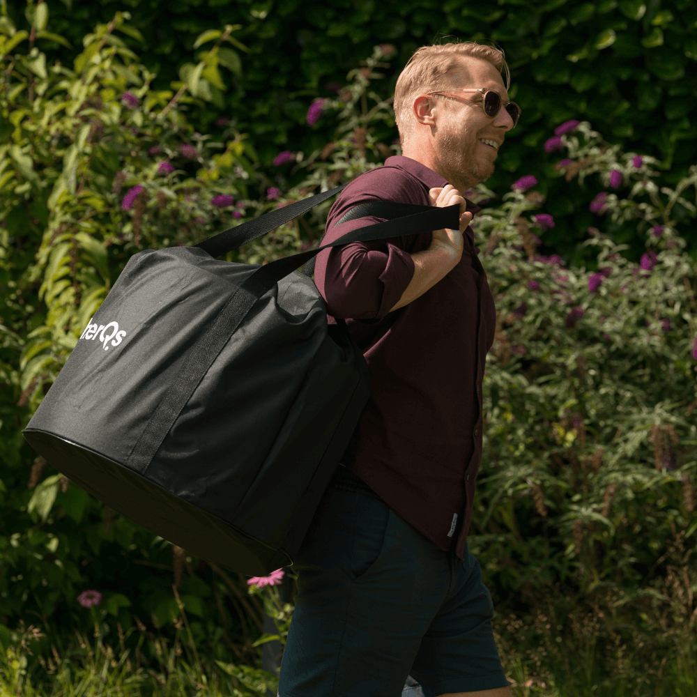Mann, der eine schwarze Tasche über der Schulter trägt, geht in einem Garten mit Büschen spazieren. Sonniger Tag.