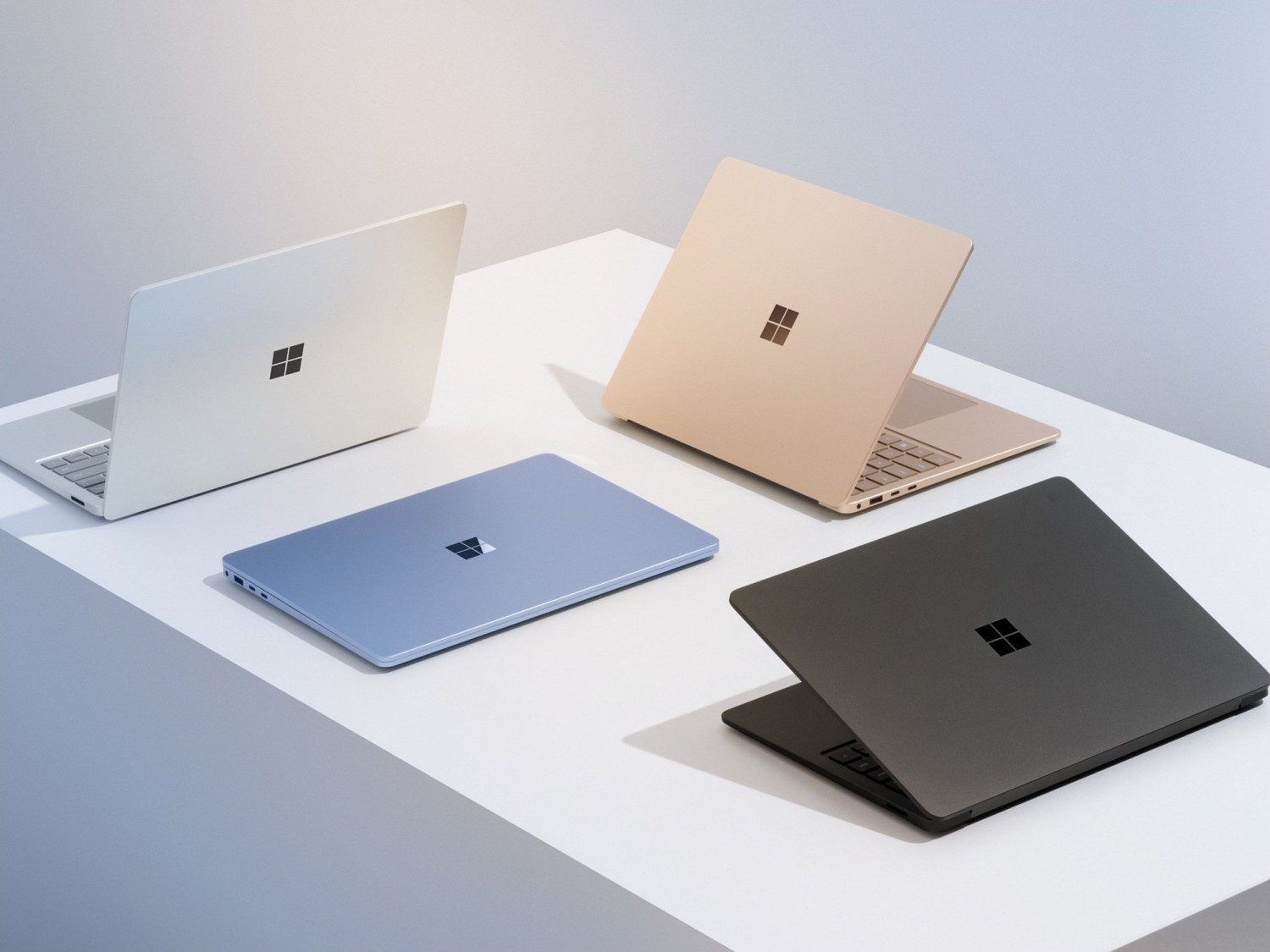 Cztery laptopy w różnych kolorach: biały, złoty, niebieski i czarny, na białej powierzchni.