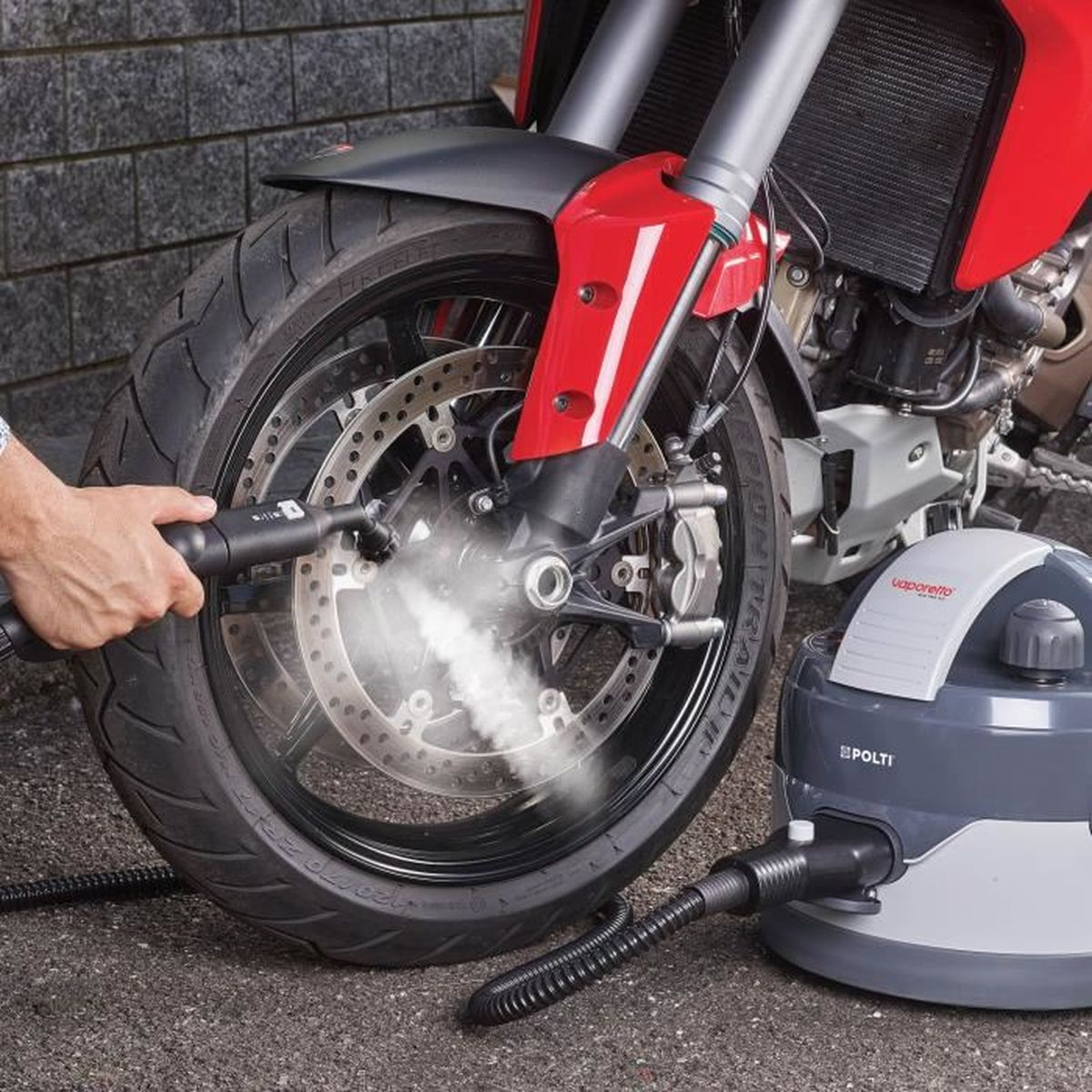 Osoba używająca parownicy do opony motocykla. Parownica stoi na ziemi.