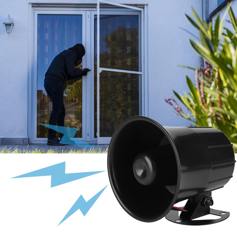Eine Person in schwarzer Kleidung bricht in ein Haus ein. Ein schwarzer Alarm im Vordergrund.