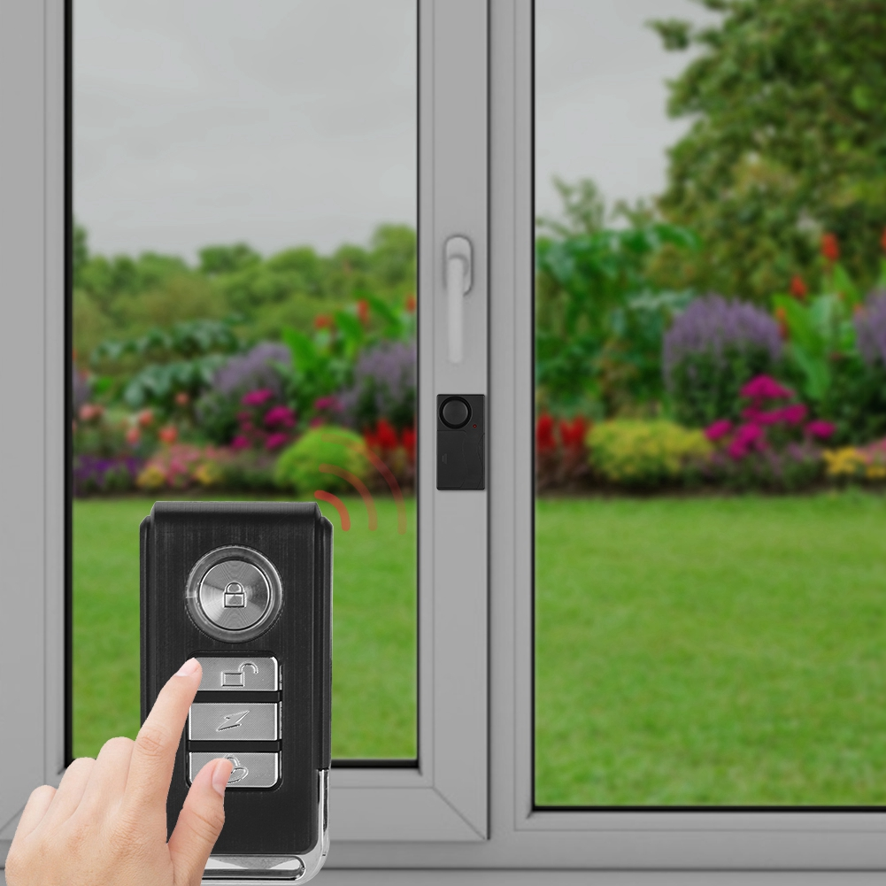 Eine Hand, die eine Fernbedienung neben einem Fenster hält, mit einem Fenstersensor am Rahmen montiert.