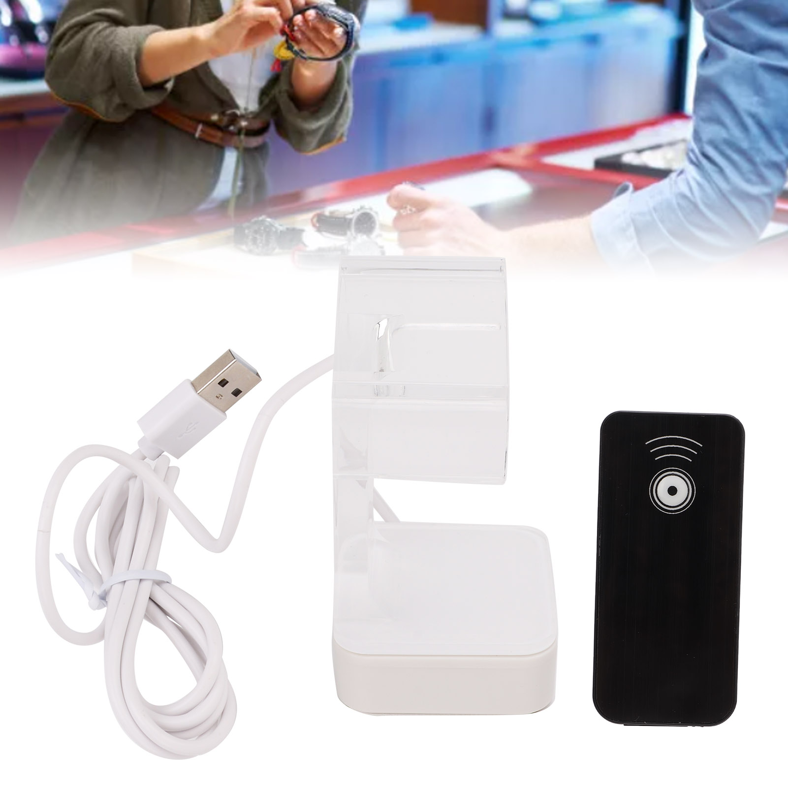 Weiße Ladestation mit USB-Kabel und schwarzer Fernbedienung. Personen sind im Hintergrund.