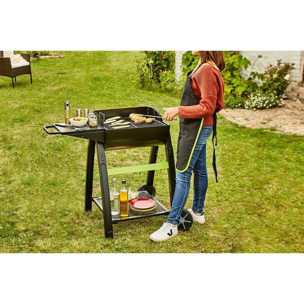 Eine Person grillt Essen auf einem Grill im Garten, mit verschiedenen Gegenständen auf einem Beistelltisch.