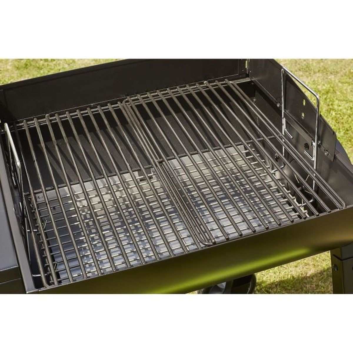 Metallgrill über einer schwarzen Grillbox. Der Grill steht auf einer grünen Grasfläche.