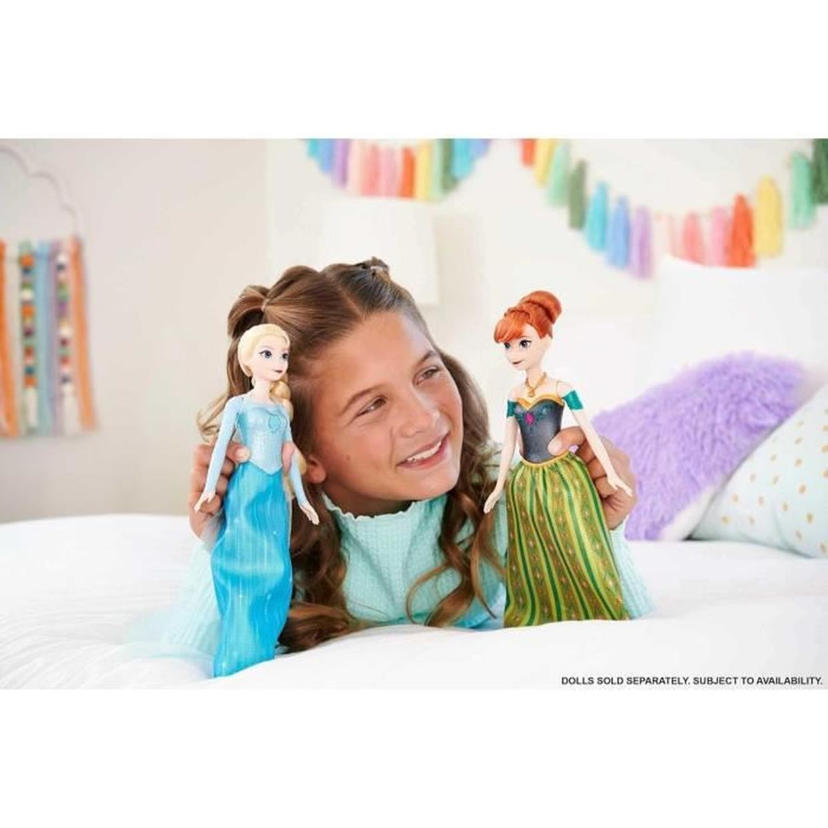 Una niña sosteniendo dos muñecas de Frozen, en un dormitorio, con texto: "MUÑECAS SE VENDEN POR SEPARADO, SUJETO A DISPONIBILIDAD".