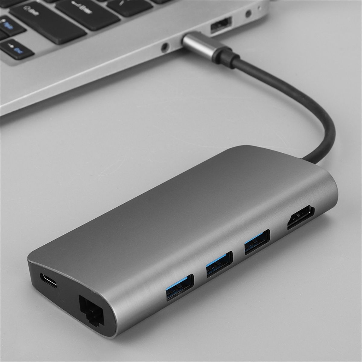 Ein grauer Hub mit mehreren Anschlüssen, der über ein USB-C-Kabel mit einem Laptop verbunden ist.