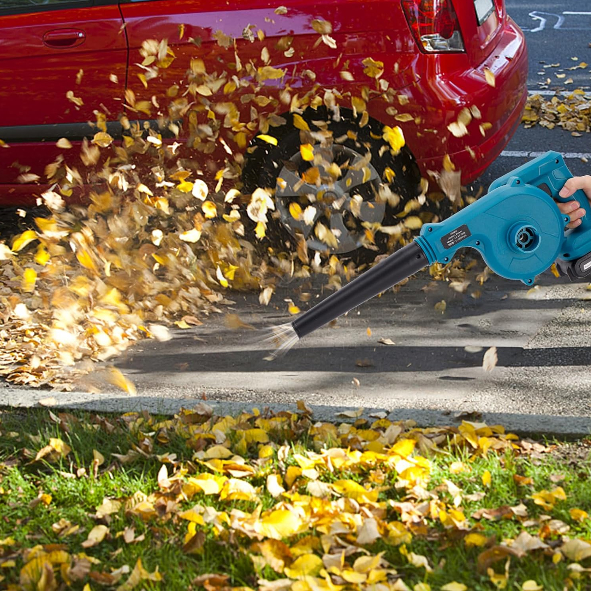 Ein Laubbläser bläst Blätter. Die Blätter sind gelb. Ein rotes Auto ist im Hintergrund.