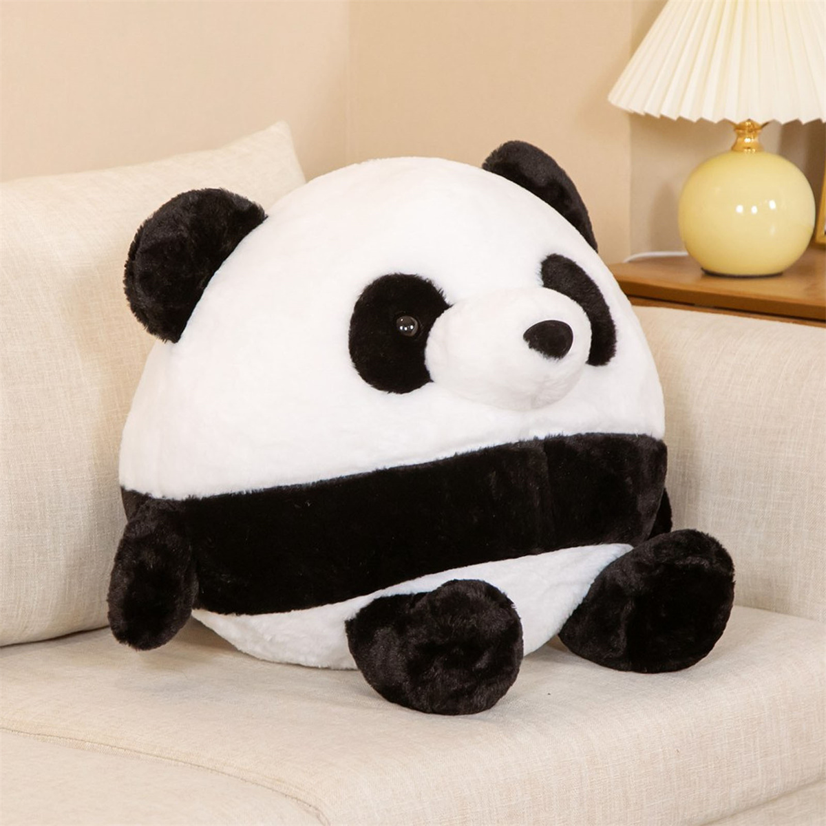 Ein Panda-Bär-Plüschtier sitzt auf einem Sofa. Es ist schwarz und weiß und rund.
