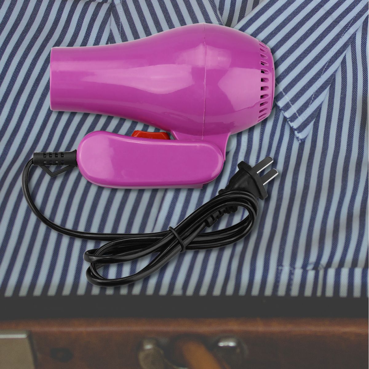 Pinkfarbener Haartrockner mit schwarzem Kabel und Stecker. Er liegt auf einem gestreiften Hemd.