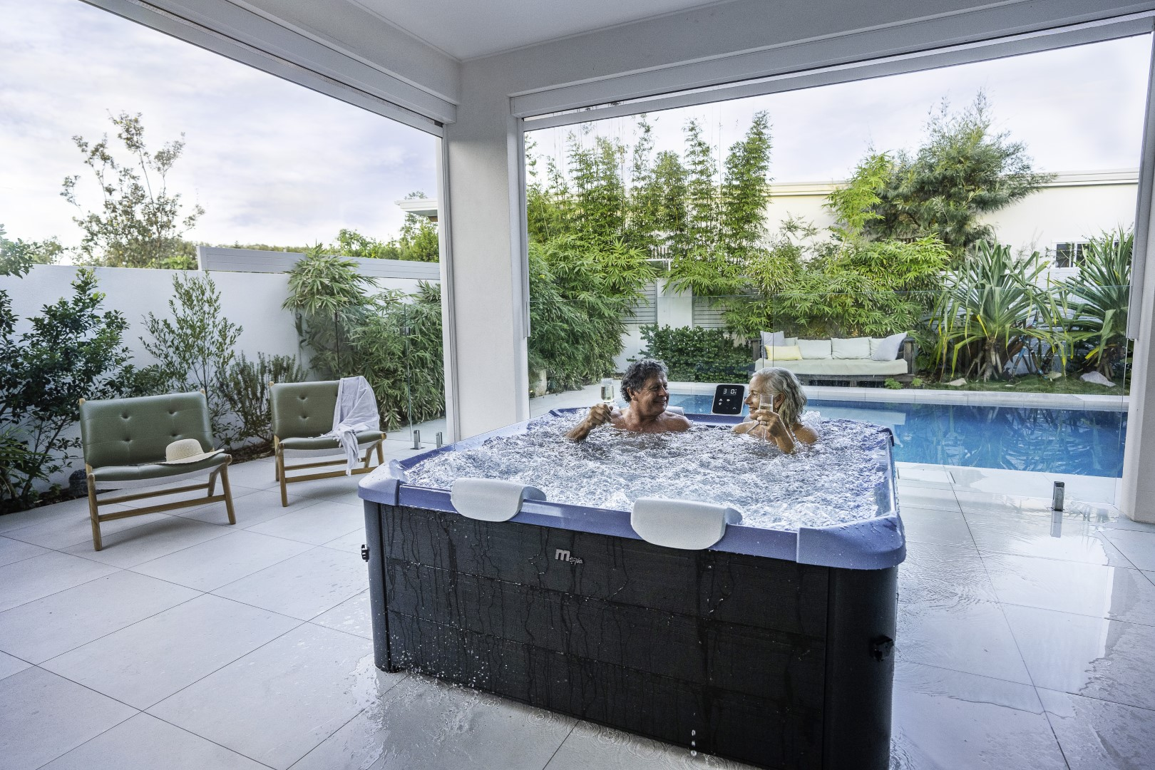 Ein älteres Ehepaar in einem Whirlpool. Sie lächeln und schauen sich an. Im Hintergrund eine Terrasse und ein Pool.