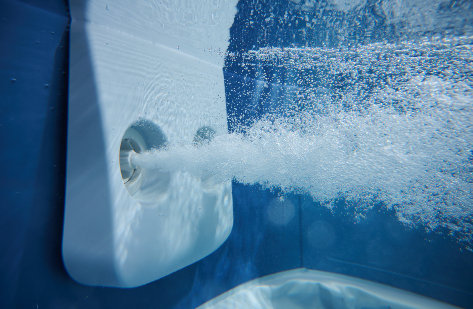 Unterwasseransicht eines Pooljets, der Blasen in blaues Wasser ausstößt.