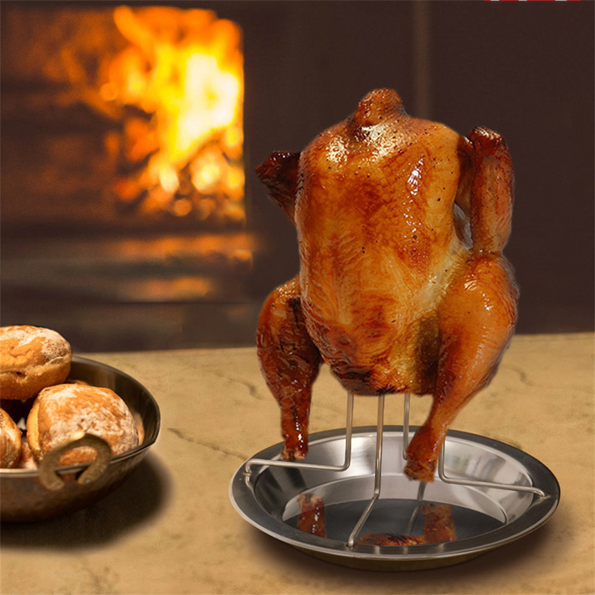Ein gebratenes Huhn auf einem Metallständer. Eine Schüssel mit Brötchen im Vordergrund, Kamin im Hintergrund.