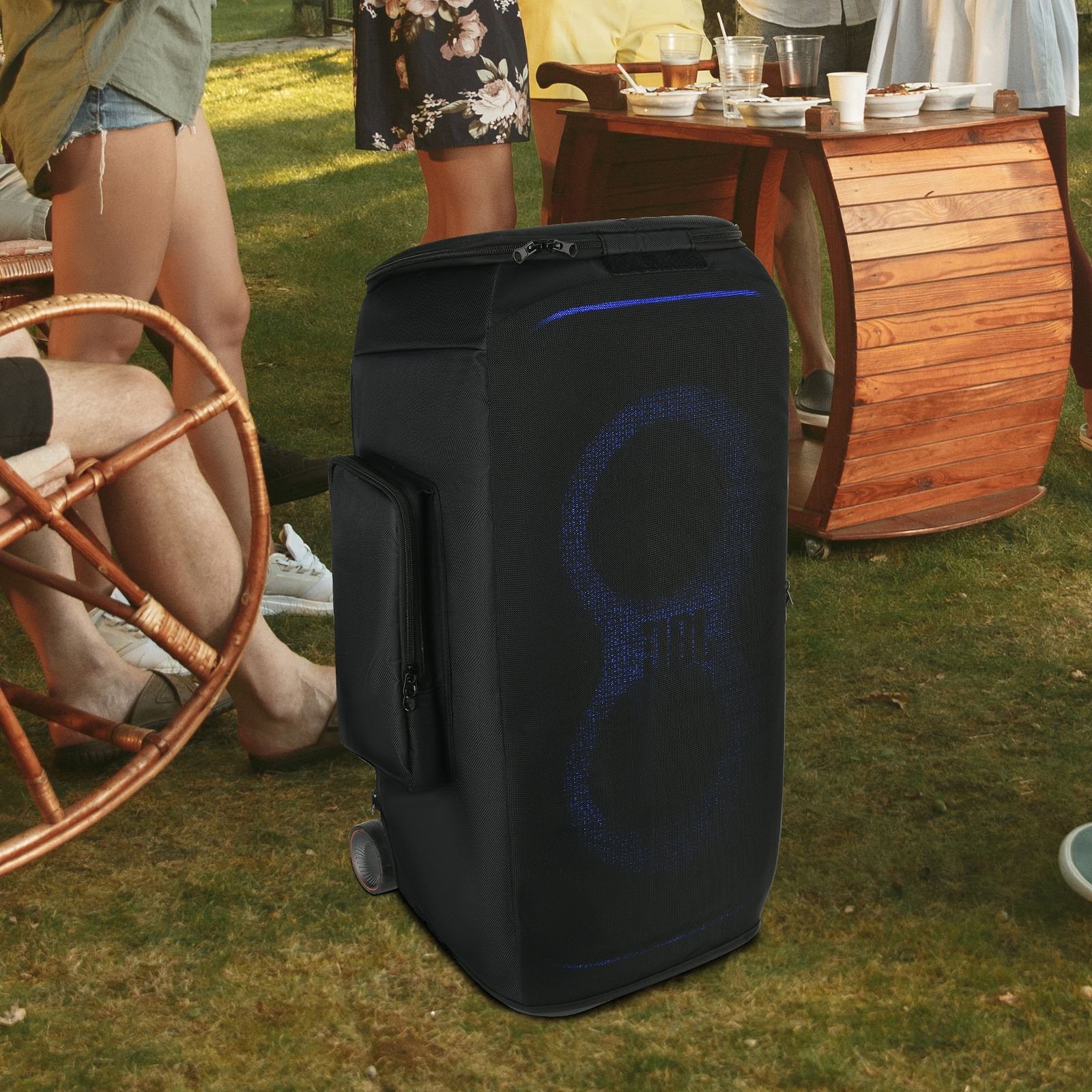 A black portable speaker on a grassy lawn, surrounded by people. A person is on a chair.