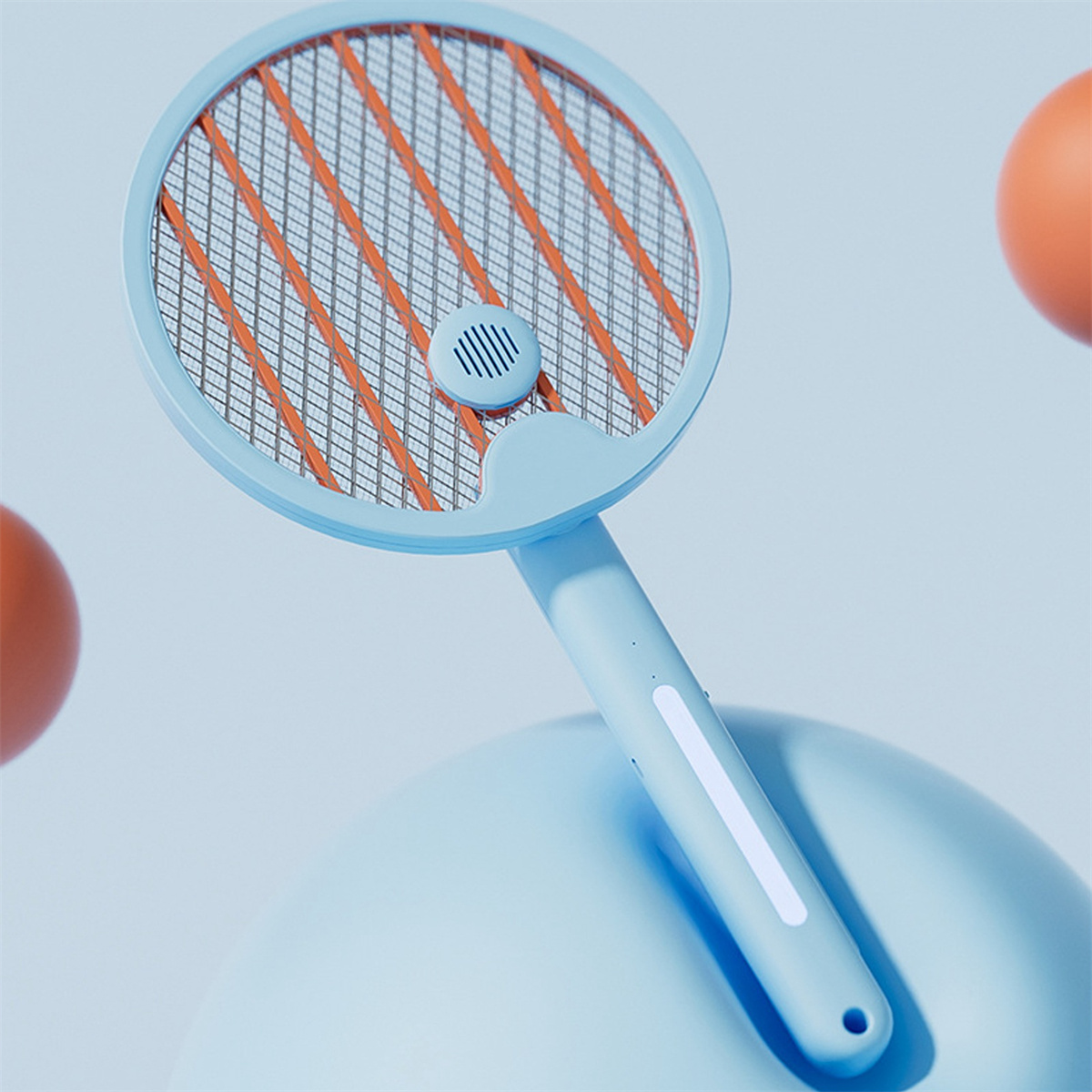 Ein blauer elektrischer Fliegenfänger mit orangefarbenem Netz und blauem Griff. Im Hintergrund sind orangefarbene Kugeln.