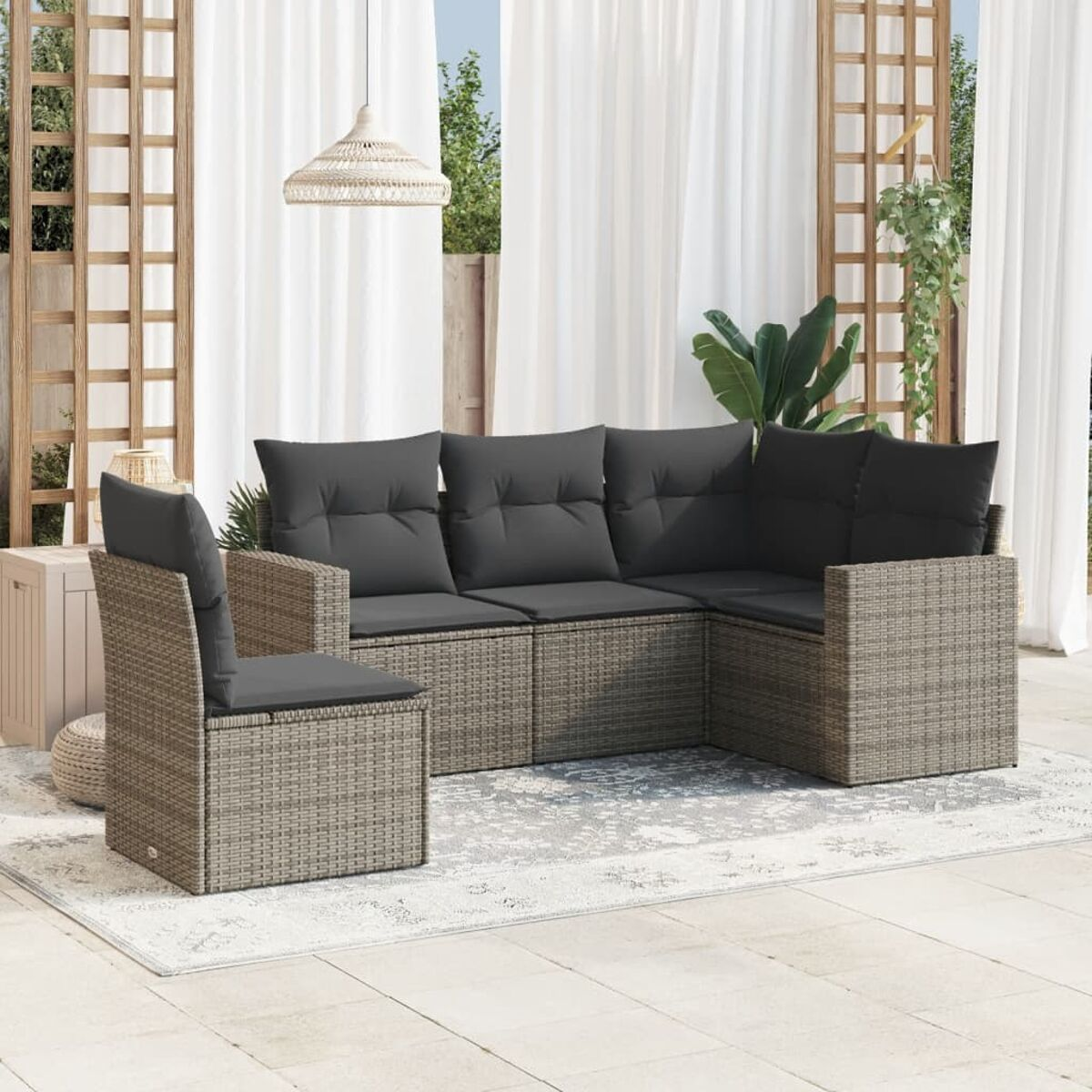 Un divano componibile da esterno in rattan con cuscini grigio scuro, su un patio con tende e una pianta.