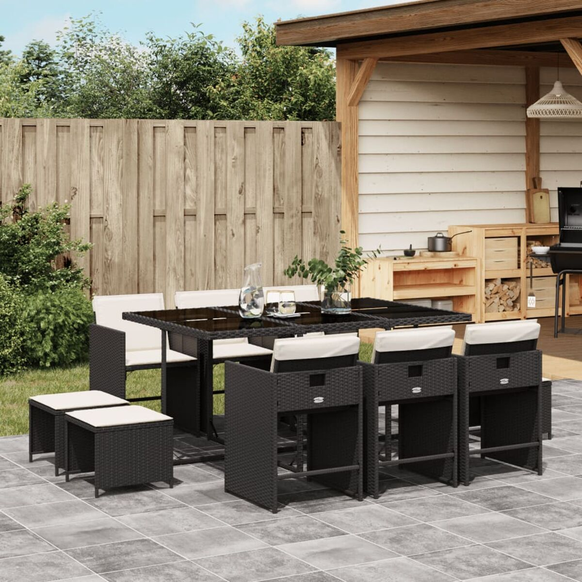 Essgruppe im Freien mit Tisch und Stühlen, auf einer Fliesen-Terrasse, mit Holzzaun und Grün.