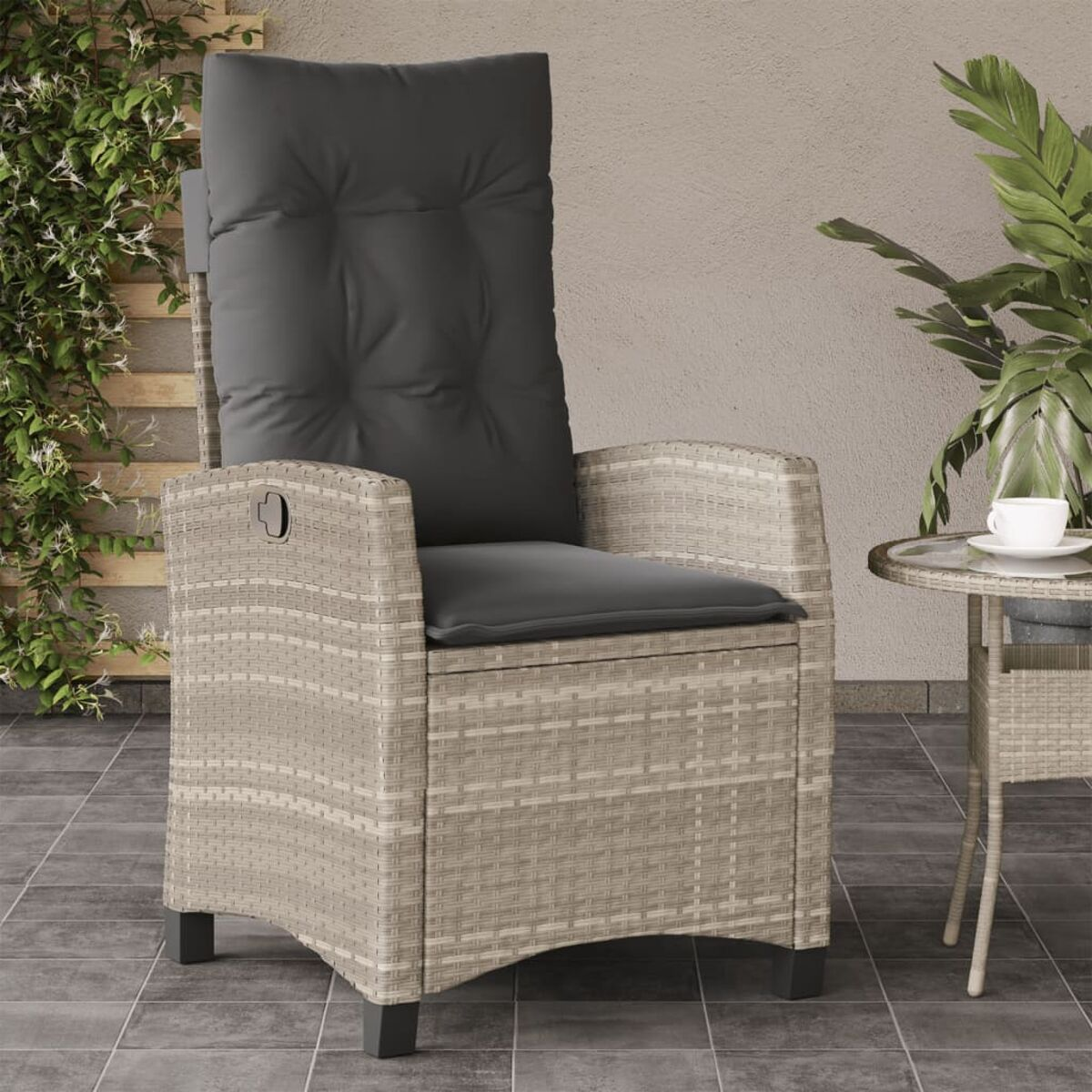 Ein Outdoor-Sessel aus Rattan mit dunkelgrauem Kissen und einem Beistelltisch mit einer Tasse, auf einer Terrasse.