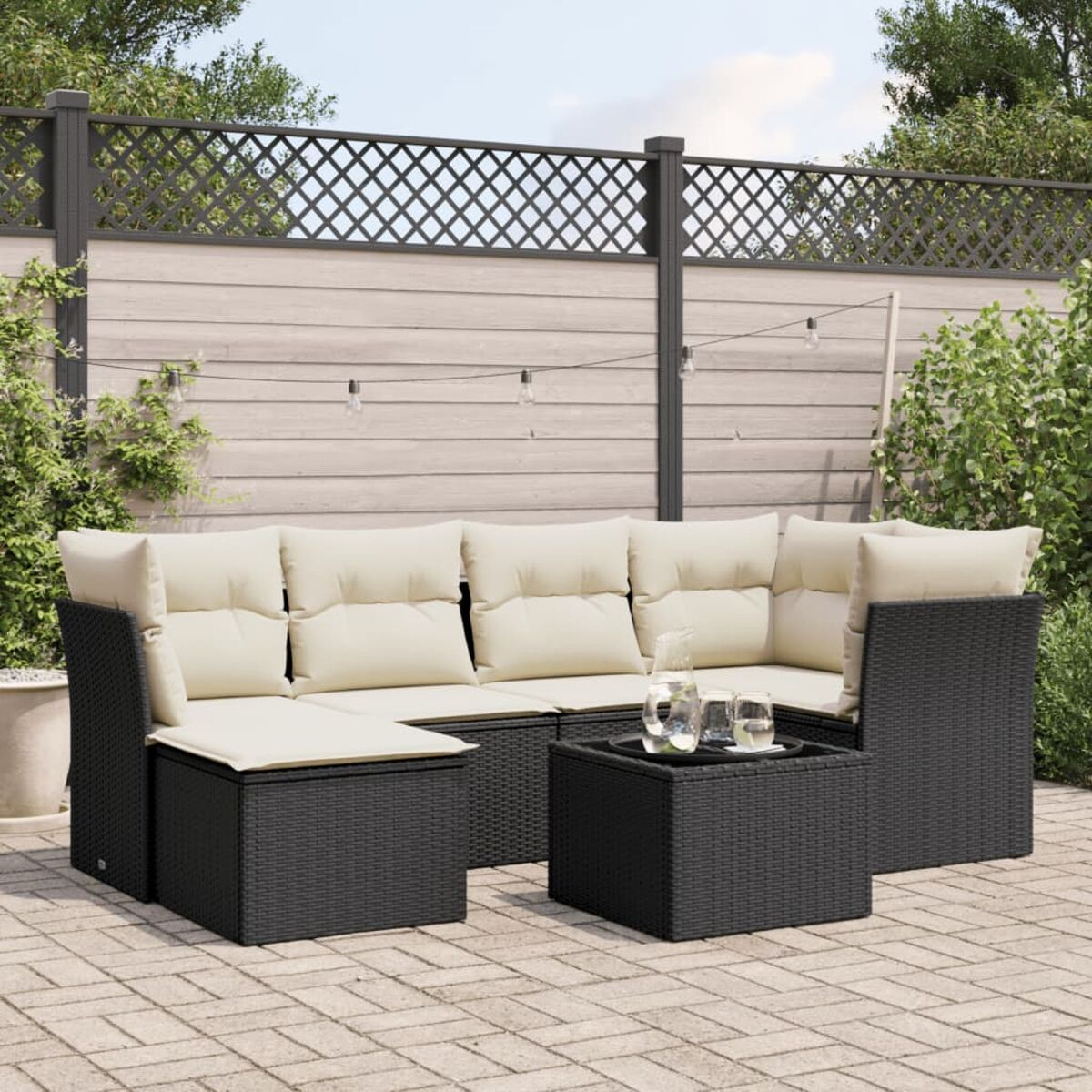 Gartenmöbel-Set im Freien. Schwarzes Korbmöbel mit beigen Kissen und kleinem Tisch, mit Pflanzen.