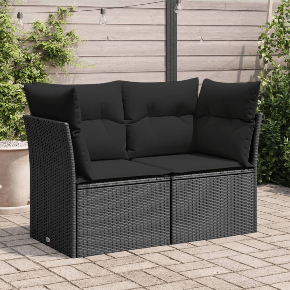 Outdoor-Sitzgruppe. Schwarzes, gewebtes Design-Sofa und zwei passende Ottomanen auf einer gepflasterten Terrasse.