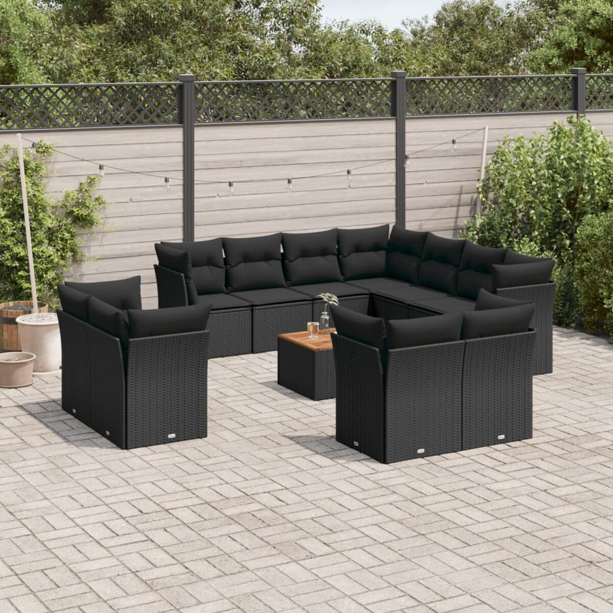 Gartenmöbel-Set: schwarze Korbsessel, Stühle, ein Tisch und Kissen auf einer Steinterrasse.