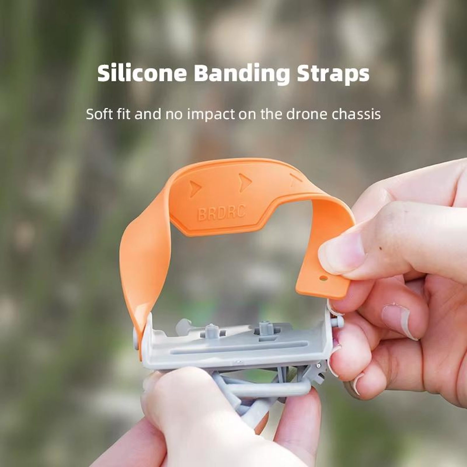 Cinghie di fissaggio in silicone arancione tenute in mano, su un telaio di drone grigio. Sfondo sfocato.