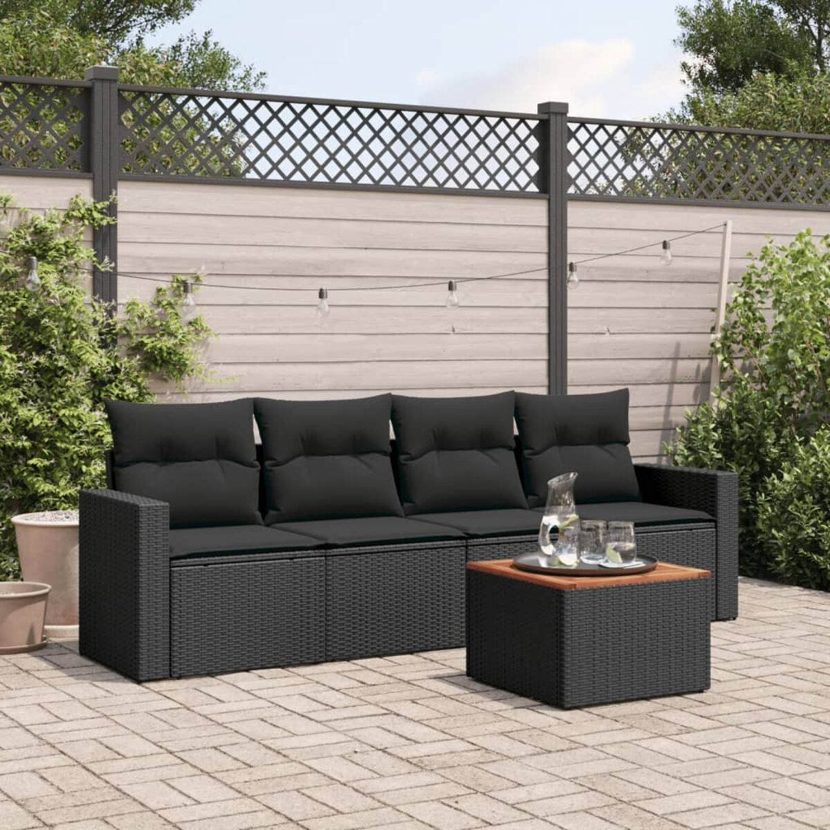 Schwarzes Outdoor-Sofa mit Kissen, Couchtisch und Holzzaun.