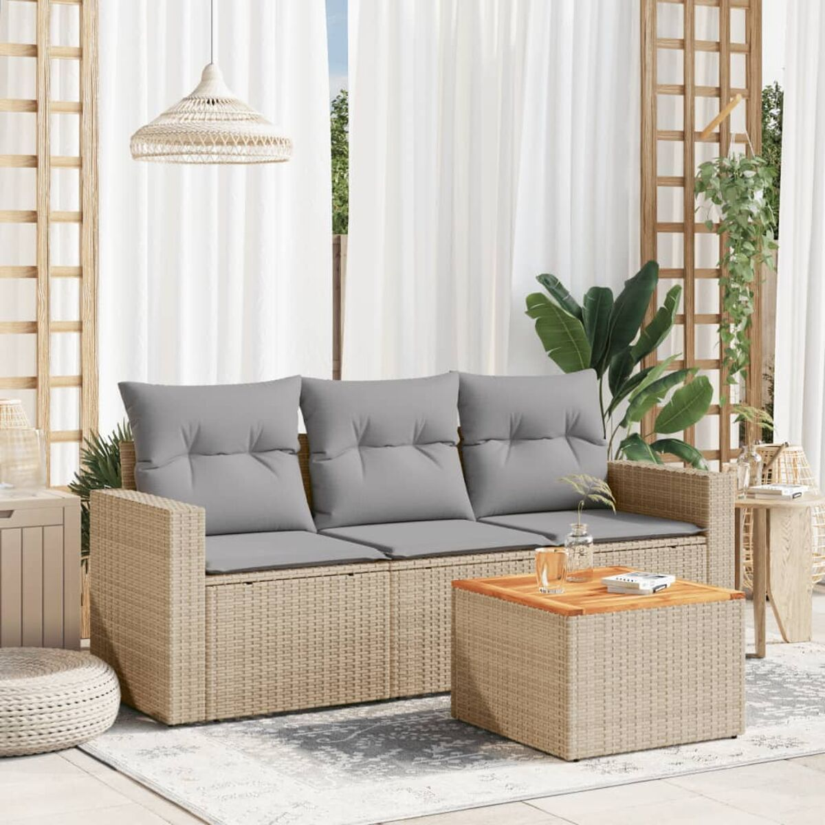 Divano in rattan con cuscini grigi, tavolino e tappeto su patio con tende e piante.