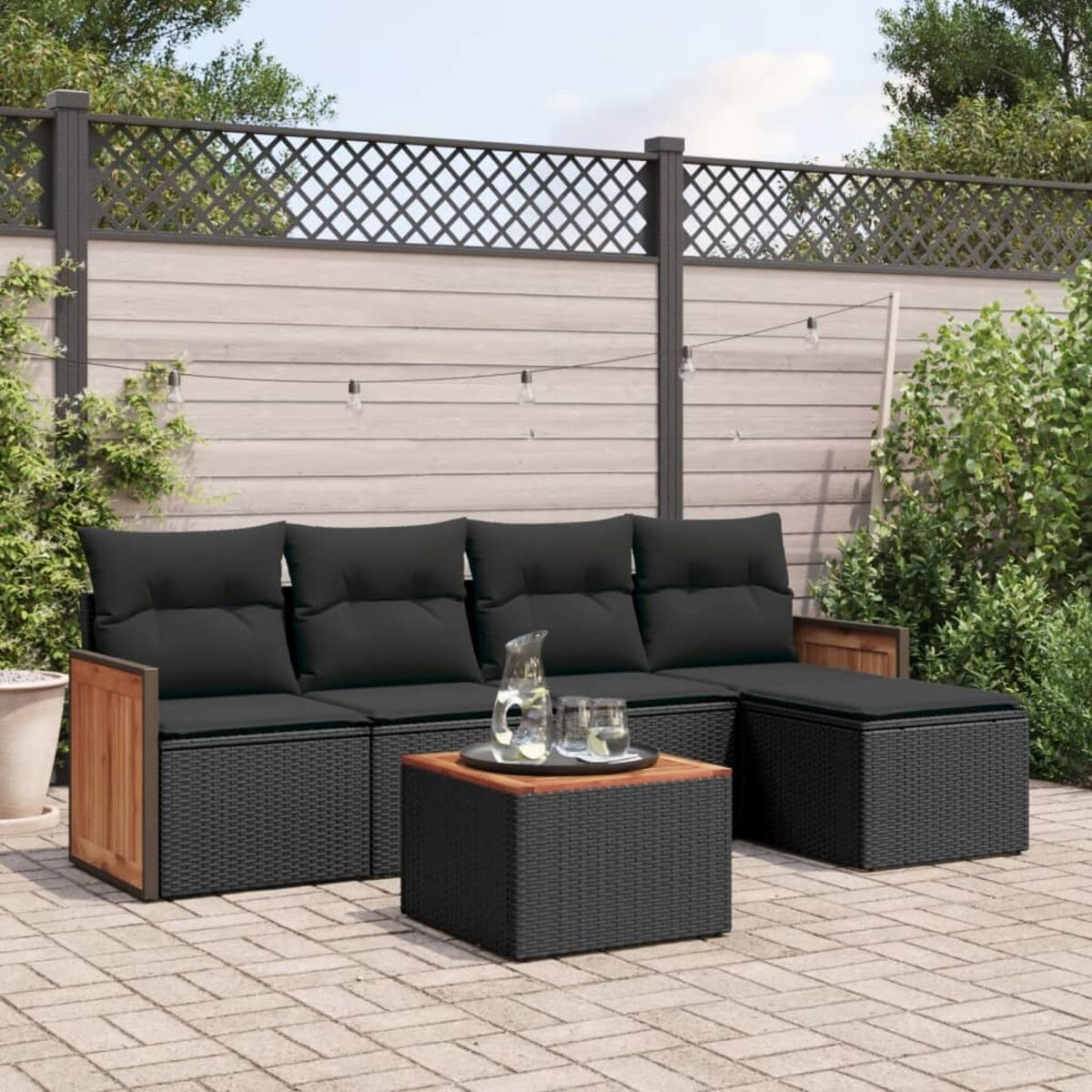 Un set di mobili da esterno neri. Include un divano, un pouf e un tavolino, il tutto su un patio in mattoni.