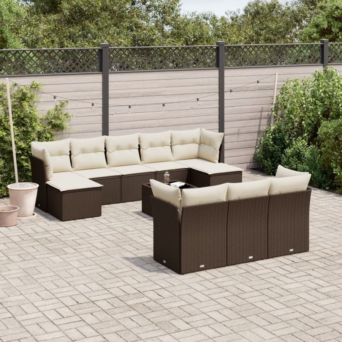 Set di sedute da esterno in vimini marrone con cuscini color crema su un patio in mattoni.