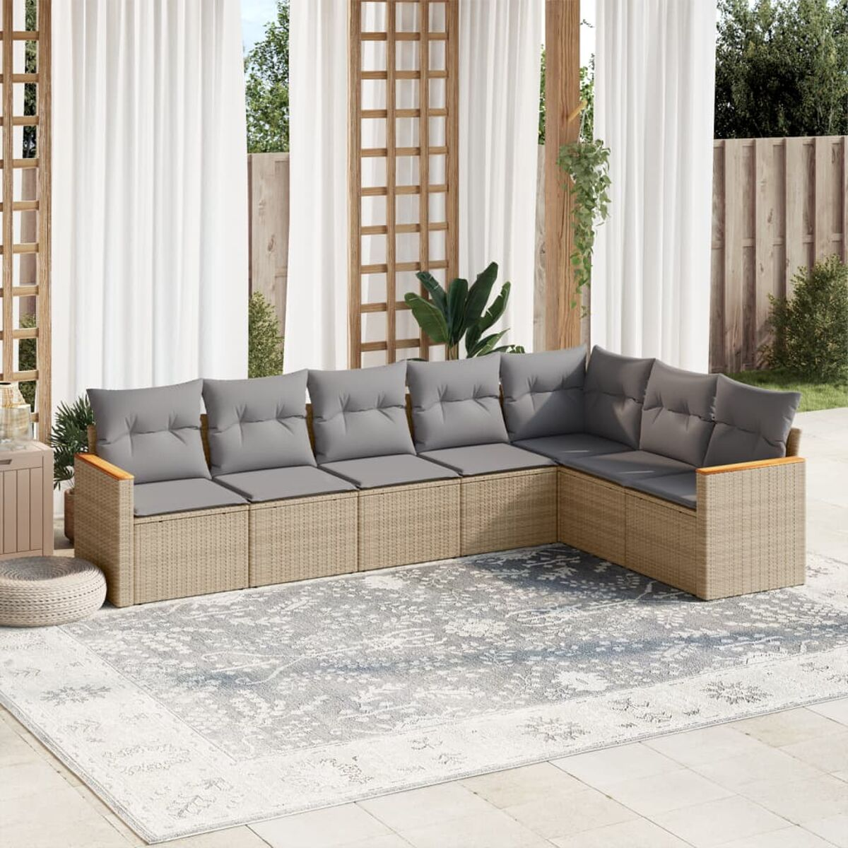 Divano angolare in rattan beige con cuscini grigi su un tappeto grigio, su un ponte di legno con tende bianche.